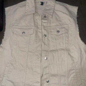beige/cremefärgad jeansväst från H&M - säljer en snygg beige/cremefärgad jeansväst från H&M i storlek S. västen har en klassisk krage och knappar framtill. väldigt enkel och snygg. den är i nytt skick och oanvänd!