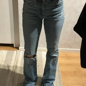 Blå jeans med slitningar - Säljer ett par blå jeans med slitningar på knäna. De har en klassisk femficksdesign och en bekväm passform. Perfekta för en avslappnad stil.
