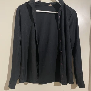 Svart långärmad skjorta - Snygg svart långärmad skjorta med knappar. Perfekt för en stilren look. Skjortan har en klassisk krage och är tillverkad i ett bekvämt material. Storleken stod inte på skjortan, men kan tänka mig att den är i S/M