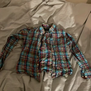 Rutig skjorta från Hackett London - Säljer en superfin rutig skjorta från Hackett London för barn i åldern 7-8 år. Skjortan har ett färgglatt rutmönster i blått, rött, grönt och gult. Den har långa ärmar och knappar framtill. Perfekt för både vardag och festliga tillfällen!