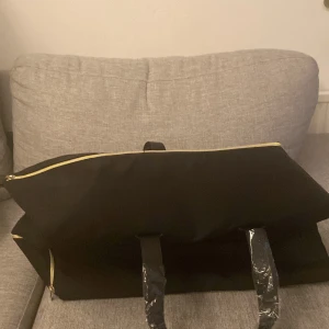 Weekendbag från Hugo Boss Parfums - Säljer en stilren svart väska från Boss Parfums. Väskan har en elegant design med guldfärgad dragkedja och svarta handtag. Perfekt för att bära dina parfymer eller andra tillhörigheter med stil. Passar både till vardags och resor. Värde 900kr. Platsen är fortfarande så du får den helt ny 