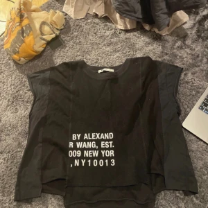 Svart t-shirt från Alexander Wang - Säljer en svart t-shirt från Alexander Wang i bomullsmaterial. Den har ett tryck på framsidan med texten 'BY ALEXANDER WANG, EST. 2009 NEW YORK, NY 10013'. T-shirten har en loose passform och korta ärmar, perfekt för en avslappnad stil. Passar bra till både vardag och fest!