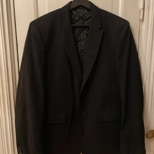 Svart kavaj från Burberry - Säljer en elegant svart kavaj från Burberry i storlek 50. Tillverkad i Italien med 91% ull och 9% polyamid, vilket ger en lyxig känsla. Kavajen har en klassisk design med knappar och en quiltad insida för extra komfort. Perfekt för höst och vinter, både till fest och formella tillfällen.