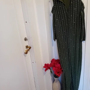 Grön glittrig långklänning från Avana - Säljer en superfin grön långklänning från Avana i storlek S. Klänningen har ett glittrigt randigt mönster och en elegant öppen axeldesign. Perfekt för festliga tillfällen! 💚✨