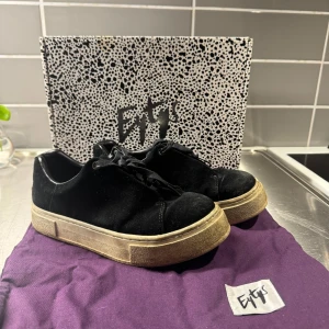 Svarta sneakers från Eytys - Snygga svarta sneakers från Eytys med en robust sula och klassisk snörning. Skorna har en stilren design med en liten lila detalj på hälen. Perfekta för en trendig look.