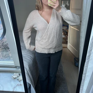 Beige omlottstickad tröja - Säljer en mysig beige omlottstickad tröja med v-ringning. Tröjan har långa ärmar och en avslappnad passform, perfekt för kyligare dagar. Den är både stilren och bekväm, ett måste i garderoben!