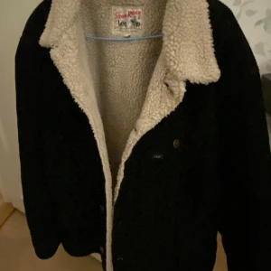 Svart jacka med teddyfoder från Lee - Säljer en svart jacka från Lee med mysigt teddyfoder. Jackan har en klassisk design med knappar framtill och en varm krage. Perfekt för kyligare dagar. Storleken är XL men jag tycker att den sitter mer som L