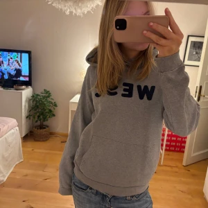 Grå hoodie med text - Säljer en grå hoodie med texteny 'WESC' i mörkblått på framsidan. Den är supermjuk och perfekt för en chill dag hemma eller ute. Har en stor ficka fram och en skön huva. Passar perfekt till jeans eller mjukisbyxor. Hör av dig om du är intresserad! 😊