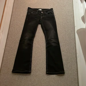 Svarta bootcut jeans - Säljer ett par snygga svarta bootcut jeans i mycket bra skick. De har vita sömmar som ger en cool kontrast och är lågmidjade för en trendig look. Perfekta för både vardag och fest!
