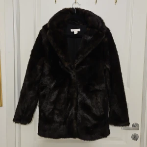 Svart/brun pälsjacka från H&M - Snygg svart/brun pälsjacka från H&M i storlek XS. Jackan har en klassisk design med långa ärmar och en mjuk, lyxig känsla. Perfekt för att hålla sig varm och stilren under kyliga dagar. Fint skick, i princip som ny.