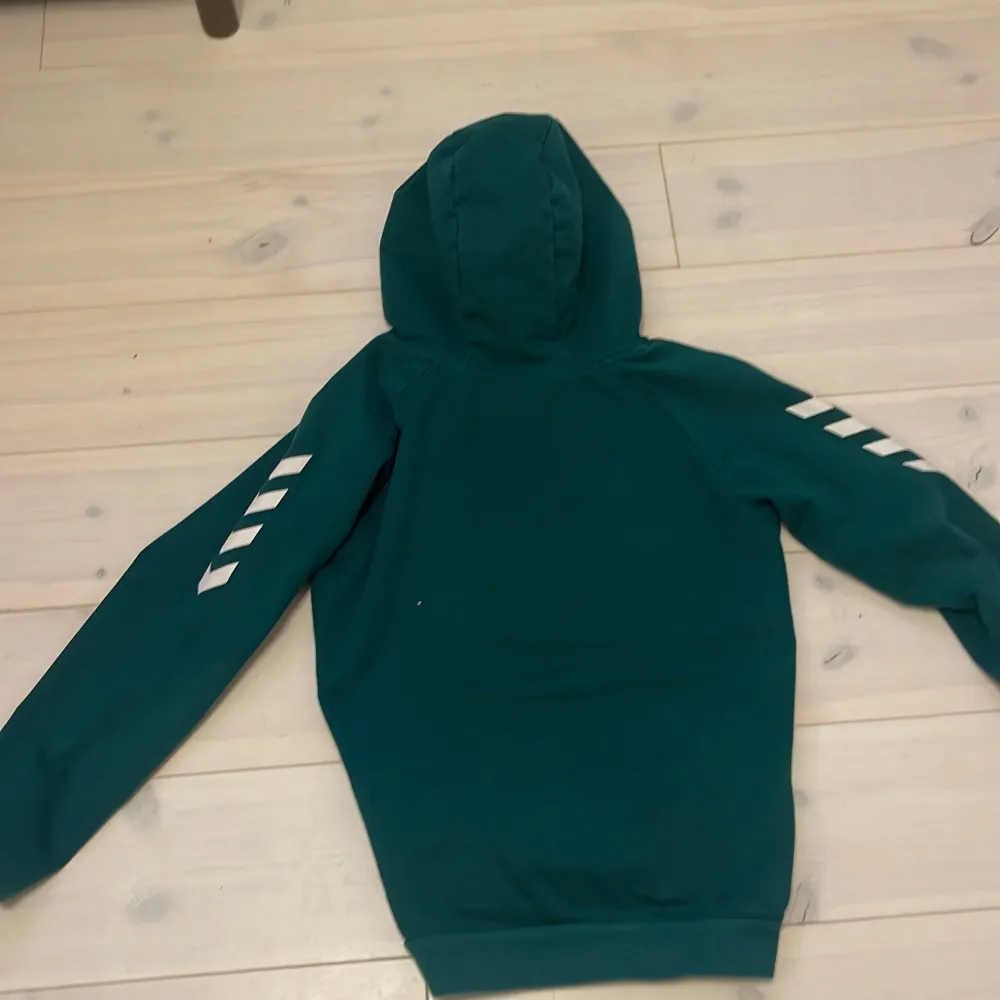 Säljer en snygg grön hoodie från Hummel i bra skick. Den har vita detaljer på ärmarna och en bekväm huva med grå insida. Perfekt för höst och vinter, och funkar lika bra till träning som till vardags. Passformen är normal och materialet känns mjukt och skönt. Hör av dig om du är intresserad!. Tröjor & Koftor.