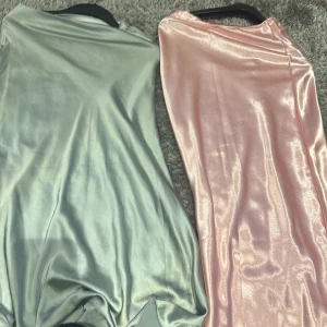 Glittriga långklänningar i silver och rosa - Två fantastiska satin kjol i glittrigt material, en i grön och en i rosa. Perfekta för festliga tillfällen med sin eleganta och skimrande look. Kjolarna har en smickrande passform och är tillverkade i ett mjukt och bekvämt material.