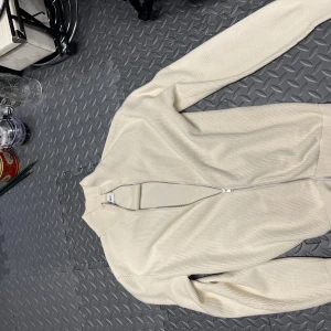Beige stickad tröja från East West - Säljer en snygg beige stickad tröja från East West. Den har en dragkedja framtill och är långärmad, perfekt för höst och vår. Säljer för lite förstora för mig. Använt runt 2 gånger och ny pris 1100 på brothers