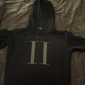 Les Deux Hoodie - Säljer en stilren svart hoodie från Les Deux med en stor grå logga på framsidan. Lite sönder på framsidan där loggan står, annars okej. Skick 7/10, sliten av färg men kan användas som vanligt. Storlek L, men sitter mer som M. Köpt från Plick för ungefär 250 kr ganska nyligen, mitt pris = 169 kr