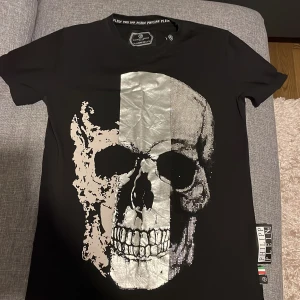 Svart t-shirt med dödskalle från Philipp Plein - Säljer en cool svart t-shirt från Philipp Plein med en stor silverfärgad dödskalle på framsidan. T-shirten är i mycket bra skick och har en normal passform. Perfekt för en avslappnad stil med en edgy touch. Storleken är M.