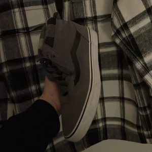 Vans vinterskor - Snygga grå sneakers från Vans med hög modell och klassisk vit sula. Skorna har snörning och en ikonisk sidostrimma i svart. Perfekta för en avslappnad stil. Bra skick använda max 2-3 gånger.