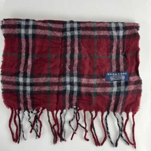 Rutig halsduk från Burberry - Säljer en superfin rutig halsduk från Burberry i rött, svart och vitt. Den är gjord av 100% kashmir och har en klassisk design med fransar i ändarna. Perfekt för att hålla sig varm och snygg under kyliga dagar. Passar både höst och vinter!