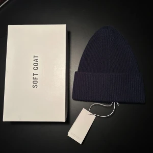 Soft Goat Mössa - Säljer en supermjuk och stilren mörkblå mössa från Soft Goat i 100% Kashmir. Den kommer med originalförpackning med etikett kvar. Perfekt för att hålla dig varm och snygg under kyliga dagar. Den är helt oanvänd då det var en present som inte passa. Kostar ca 1000 kr ny. 