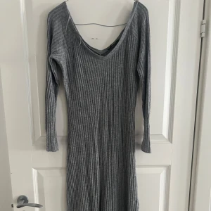 Grå ribbad klänning från Bik Bok - Snygg grå ribbad långklänning från Bik Bok med v-ringning och långa ärmar. Perfekt för en stilren look med en liten slits för extra rörelsefrihet. Passar bra till både vardag och speciella tillfällen.