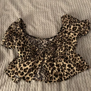 Leopardmönstrad blus - Trendig leopardmönstrad blus med korta ärmar och volangdetaljer. Knytdetalj på mitten