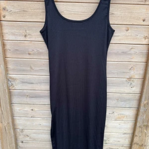 Svart ribbad klänning - Snygg svart ribbad klänning med ärmlös design och en stilren slits på sidan. Perfekt för en chic och minimalistisk look. Klänningen har en normal passform och är gjord i ett bekvämt material.