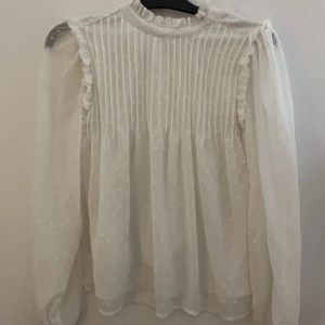 En fin vit blus - En vit blus med fina prick detaljer. Med mech genomskinliga armar. Perfekt för en sommar fest. Eller kanske en skolavslutning! 