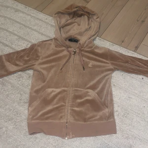 Beige hoodie från Juicy Couture - Säljer en snygg beige hoodie från Juicy Couture. Den har en dragkedja framtill och en justerbar huva med snören. Materialet är mjukt och skönt, tillverkat av polyester och elastan. Perfekt för en avslappnad stil. I storlek XXS🫶🏻