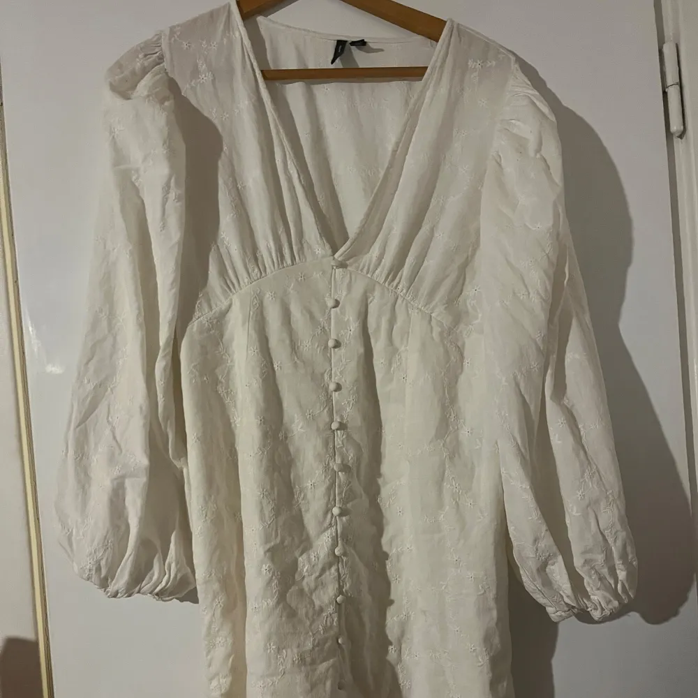 Säljer en vacker vit klänning från Vero Moda med broderade blommor och knappar framtill. Klänningen har långa ärmar och en v-ringad uringning. Köpt här på plick, är i otroligt bra skick!😊💕. Mekot.