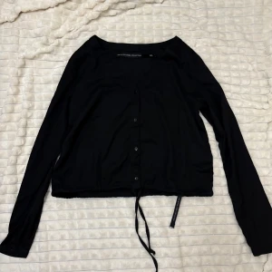 Svart kofta från NA-KD - Snygg svart blus  med knappar framtill och knytband i nederkant. Så den kan justeras för att sitta högre vilket efterlikna en magtröja