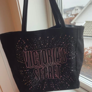 Svart shoppingväska från Victoria's Secret - Snygg svart shoppingväska från Victoria's Secret med ett glittrigt mönster och stort tryck på framsidan. Väskan har två handtag och en praktisk innerficka. Helt ny men inte kommit till användning. Pris kan diskuteras 🥰