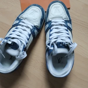 Blå och vita sneakers från Louis Vuitton - Vi kan snaka om priset vid köp.        Snygga sneakers från Louis Vuitton i blått och vitt. Skorna har en klassisk design med snörning och märkets logotyp på sidan. Perfekta för den som vill ha en stilren look med en touch av lyx.