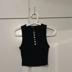 Svart ärmlös topp från Paulmark - Snygg svart ärmlös topp från Paulmark i storlek S. Toppen har knappar framtill och en stilren design som passar perfekt till olika outfits. Perfekt för varma dagar eller som ett lager under en jacka.