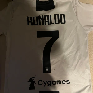Juventus fotbollströja med Ronaldo 7 - Säljer en Juventus fotbollströja från Adidas med Ronaldo och nummer 7 på ryggen. Tröjan är vit och svart med korta ärmar och har Juventus-loggan samt Jeep som sponsor på framsidan. Perfekt för fans av Ronaldo och Juventus!