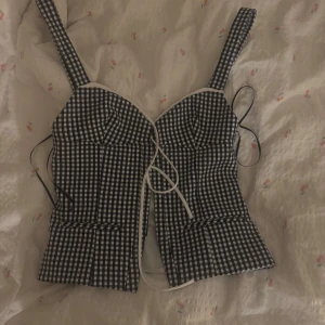 Svartvit rutig korsettopp - Snygg svartvit rutig korsettopp med breda axelband och knytning framtill. Man knäpper de fram till! Aldrig använd endast prövad.