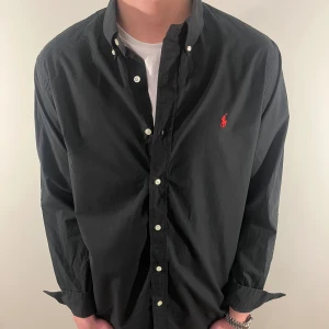Svart Ralph Lauren skjorta - Nu säljer vi ännu en fet polo skjorta som passar till alla tillställningar och skjortan är i mycket bra skick! Du ska kunna uttrycka stil utan att det kostar för mycket!🕺🍾💼🤩  Storlek👔: L Nypris💰: 1499kr