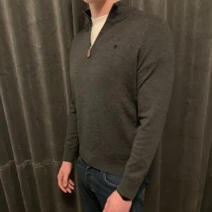 Grå merinoulltröja från Morris - Säljer en stilren grå tröja från Morris i 100% merinoull. Tröjan har en dragkedja vid halsen och långa ärmar, perfekt för kyligare dagar. Den är både bekväm och snygg, ett måste i garderoben!