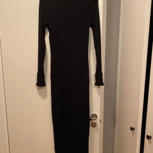 Svart långklänning från ASOS Design - Elegant svart långklänning från ASOS Design. Klänningen har en figurnära passform och långa ärmar, perfekt för en stilren look. Tillverkad i ett mjukt och bekvämt material som ger en smickrande siluett.