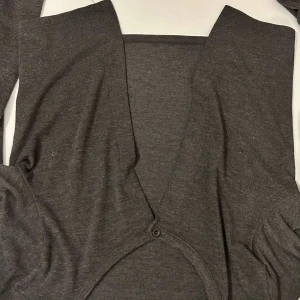 Grå kofta med knappar - Säljer en stilren grå kofta med knappar framtill. Perfekt för lager-på-lager och passar till många olika outfits. Koftan har långa ärmar och är tillverkad i ett mjukt material. den har ett litet hål i en av armarna 