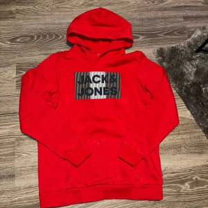 Röd hoodie från Jack & Jones - Säljer en snygg röd hoodie från Jack & Jones med ett coolt tryck på framsidan. Perfekt för en avslappnad stil. Hoodien har långa ärmar och en klassisk känguruficka framtill. Passar perfekt för kyligare dagar.