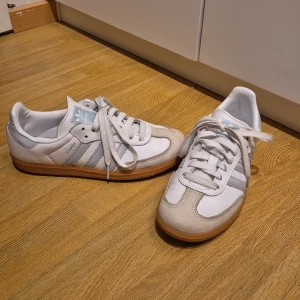 Vita Adidas Samba sneakers str 37 1/3 - Använda fåtal gånger då de va för små för mig. Snygga vita Adidas Samba sneakers med klassiska tre ränder i ljusgrått. Skorna har en gummisula i brunt och snörning framtill. Perfekta för en sportig och stilren look.