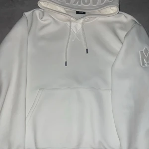 Vit hoodie från Mackage - Säljer en stilren vit hoodie från Mackage med en broderad logga på ärmen. Den har en klassisk känguruficka och justerbar huva med snören. Perfekt för en avslappnad look. Pris går att diskutera ✅