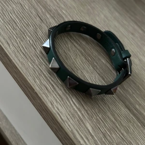 Mörk Grönt Valentino Armband - Snyggt grönt valentino armband med silverfärgade pyramidnitar. Inga defekter. Armandet har ett klassisk spänne och är tillverkat i skinn