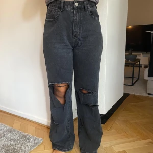 Svarta jeans med slitningar från Shein - Säljer ett par svarta jeans från Shein i storlek M. De är högmidjade och har en straight passform. Jeansen har coola slitningar på framsidan av benen, vilket ger dem en trendig look. Perfekta för en avslappnad stil!