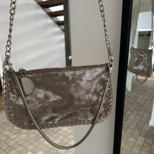 Skimmrig liten väska - Väldigt festlig väska som har en skiftande nyans av silver och ”mässing”, köpt på Sellpy. Har en liten defekt vid bandets början och det silvriga är lite avskavt därav det låga priset💕annars bra skick 