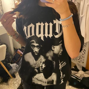 Svart T-shirt med Tupac-tryck - Säljer en svart T-shirt med ett stort tryck av Tupac Shakur och texten 'All Eyez On Me',perfekt för vardagsbruk. 