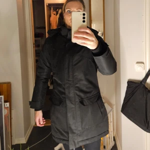 Parkas höst/vinter - Några av funktionerna är justerbar fast huva, kritiskt tejpade sömmar och tvåvägsdragkedja. Parkan är utrustad med ett vind- och vattenresistent membran som också släpper ut överskottsvärme. Denna modell är också vadderad för att klara lägre temperat