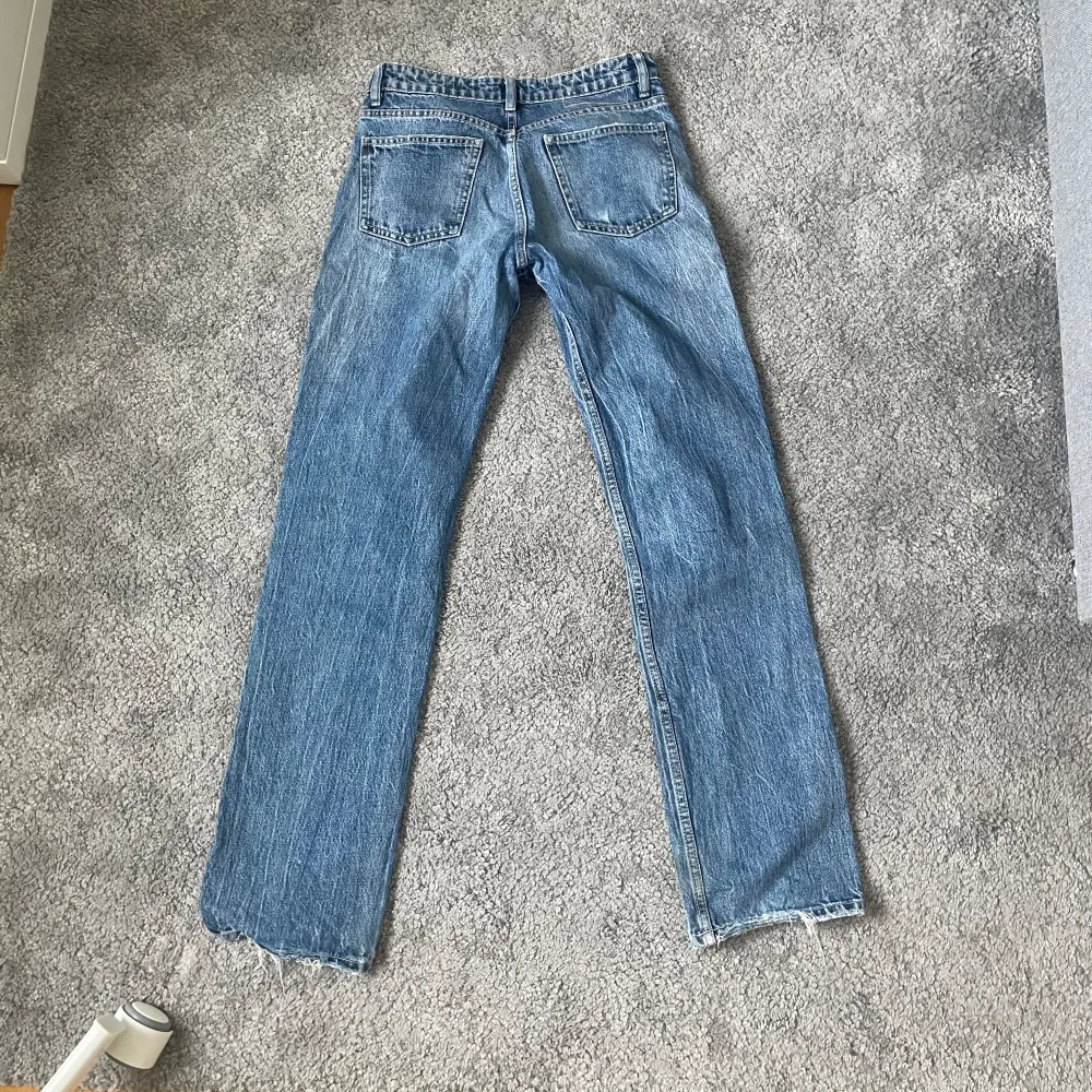 Säljer ett par klassiska blå jeans från Zara i storlek XS. De har en straight passform och är perfekta för vardagsbruk. Jeansen är tillverkade i Bangladesh och har en snygg, enkel design med fem fickor och knappgylf.. Jeans & Byxor.