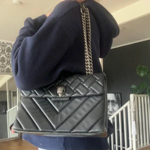 Svart quiltad axelväska från Kurt Geiger - Säljer en snygg svart axelväska från Kurt Geiger.(st medium) Väskan är quiltad med ett coolt mönster och har en kedja som axelrem. Den är perfekt för både vardag och fest. Väskan är i skinn och har en stilren design med en liten logga framtill. Bra skick förutom slitage vid under kant sidor, tycker ej de syns vid användning (ai)