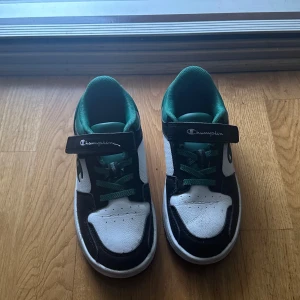Svartvita sneakers från Champion - Säljer ett par snygga svartvita sneakers från Champion. De har en cool design med gröna detaljer och snörning. Perfekta för vardagsbruk eller träning. Skorna är i bra skick och redo för nya äventyr! storlek 33
