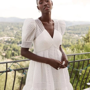 Vit klänning med spetsdetaljer - Superfin vit klänning med spetsdetaljer och puffiga kortärmar. Den har en v-ringad design och en volangkant längst ner. Perfekt för stundent eller midsommar! Har inga bilder på mig då den är för stor